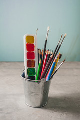 Drawing accessories - pencils, paints and brushes on a gray background