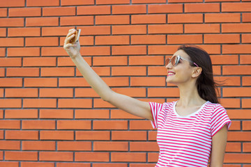 Beautiful stylish girl making selfie on brick wall background