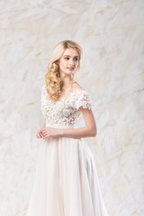 fashionable wedding dress, beautiful blonde model, bride hairstyle and makeup concept - romantic young woman in luxury white gown indoors on light background, perfect female posing in the studio
