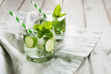Summer refreshing detox cocktail. Water with cucumber,mint  and ice in glass on a white wooden background. Rustic style.