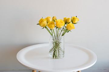 Yellow roses in glass jar on round table