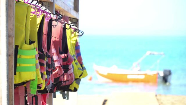 Watersport adventure background video - colorful life vests on a beach rack with a boat and waves in the background