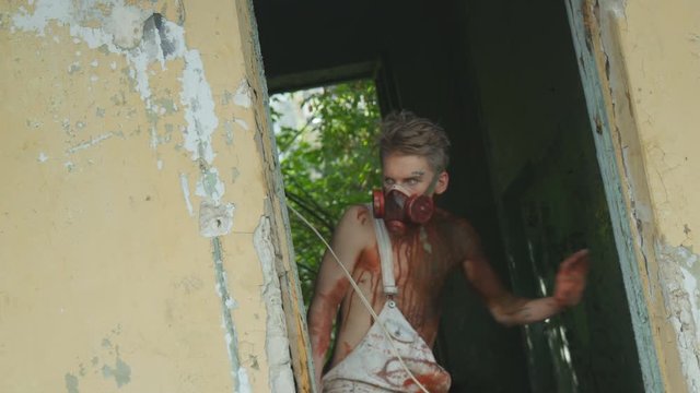 Bloody crazy guy look out of the doorway of an abandoned house