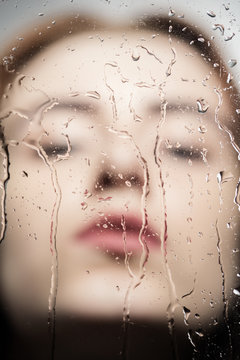 female blurred face closed eyes through glass with water drops