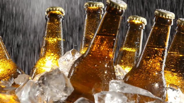 Beer stands in the ice, water flows from above, splashes fall on the glass. Black background. Close up