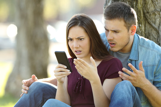 Angry couple using a smart phone outdoors