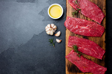 Fresh raw meat beef steaks. Beef tenderloin on wooden board, spices, herbs, oil on slate gray background. Food background with copy space