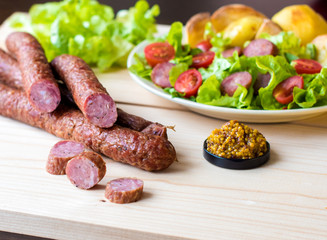 Smoked sausage with vegetables salad on a wooden board