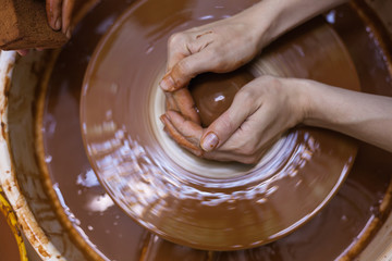 Women's hands mold the clay. Work in the pottery workshop. The Potter's wheel in operation. Top view of working process in the pottery workshop.