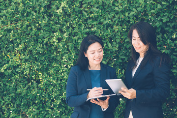Fototapeta premium Two business people discussing information on a tablet-and taking notes as they work together as a team in the garden.