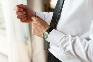 Naklejka premium Businessman adjusting his cuffs on the sleeves white shirt. Portrait of a man who straightens his cufflinks. On a hand expensive watch. Against the background of an expensive hotel. close-up.