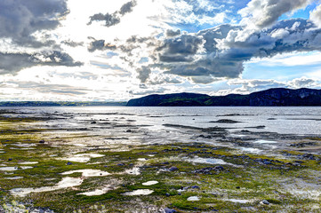 Fjord in Saguenay river closeup of beach shore with shallow water and cloudy sky