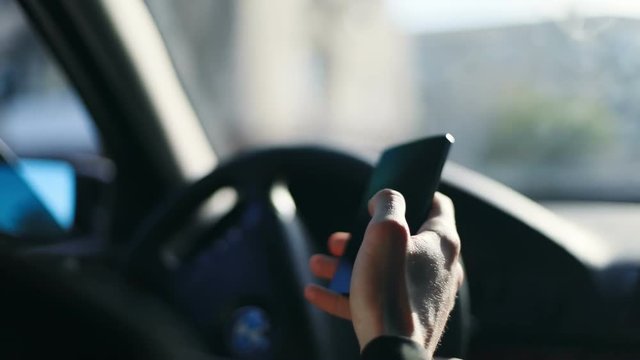 Close up man hand holding using smartphone mobile phone driving car black screen touching tapping blurred background focused hands steering gear busy dangerous networking technology driver drive