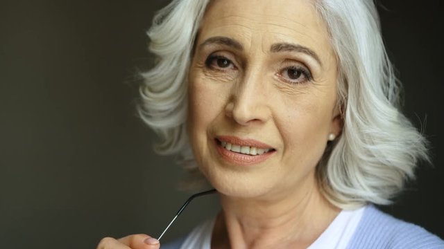 Close up portrait of beatiful old woman with eyeglasses smiling and looking at camera. Indoor shot.