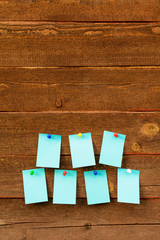 Seven empty blue paper with colorful pins over wooden background with copy space, vertical shot