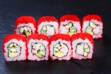 Sushi rolls with crab meat, cucumber and avocado, covered with red caviar, served on black stone slate. Restaurant menu, Japanese food art
