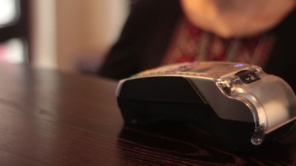 Hand Swiping Credit Card On POS Terminal. Man’s hand pushing the button and swipe credit card payment on pos terminal standing on wooden desk. Transactions at the credit card terminal.