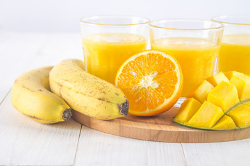 Yellow smoothie of mango, banana and orange on a white wooden table.
