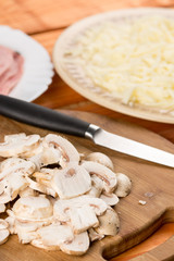 Sliced mushrooms on the round wooden board with sliced ham and cheese in the background