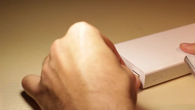 Hands of a male connect the USB cable to a white Power Bank (powerbank, batery) and phone