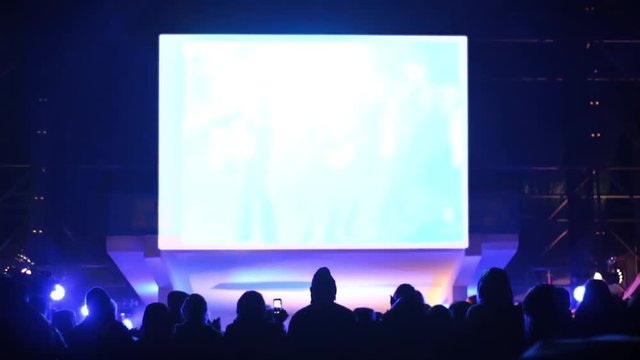 A crowd of people at the concert watches the performance. Artists on stage dance and sing songs. Above Scoreboard for capturing and displaying video. White background instead of green.