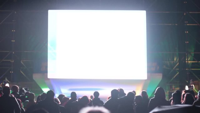 A crowd of people at the concert watches the performance. Artists on stage dance and sing songs. Above Scoreboard for capturing and displaying video. White background instead of green.