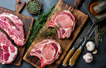 Raw pork cutlet chop for fry on grill and pan with herbs, garlic on wooden boards, slate gray background - obrazy, fototapety, plakaty