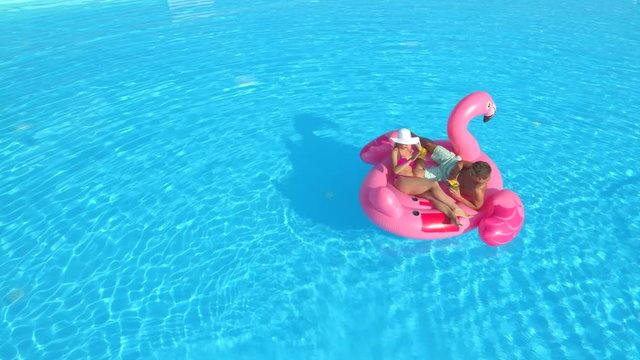 AERIAL: Funny video of couple getting rid of annoying bee while trying to relax on inflatable flamingo float. Man and woman shooing flies and wasps of their cocktail drinks on pink flamingo, hilarious