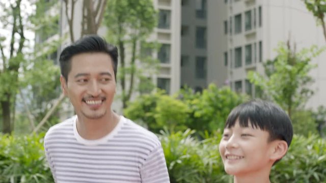 close up of Asian father & son running in garden smiling at each other in slow motion