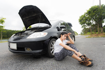 Woman sitting on the countryside road with broken car