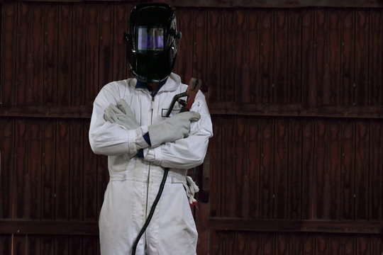 Portrait of smart welder man with torch and protective helmet in white uniform in the factory. Industrial concept. - Powered by Adobe