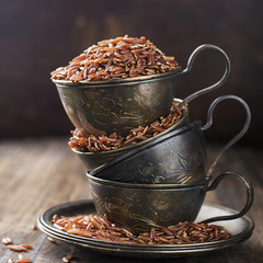 Red rice in vintage silver cups on an aged wooden background. Selective focus.