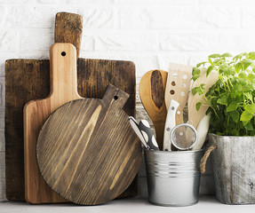 Kitchen still life on a white brick wall background: various cutting boards, tools, greens for cooking, fresh vegetables. Selective focus.
