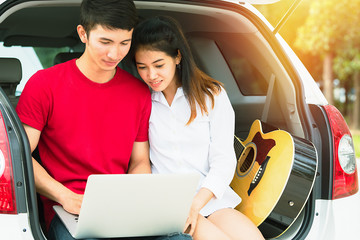 Couple sweet seated behind of car searching locations on laptop with guitar in Pattaya Thailand.