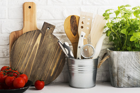 Kitchen still life on a white brick wall background: various cutting boards, tools, greens for cooking, fresh vegetables. Selective focus.