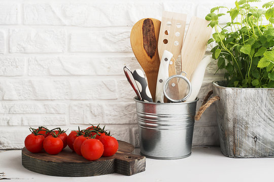 Kitchen still life on a white brick wall background: various cutting boards, tools, greens for cooking, fresh vegetables. Selective focus.