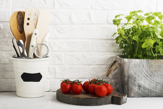Kitchen still life on a white brick wall background: various cutting boards, tools, greens for cooking, fresh vegetables. Selective focus.