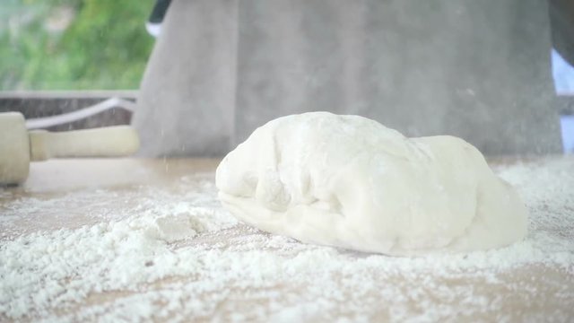 Female cook throws down loaf a dough and kneading on a table with green tree blurred background