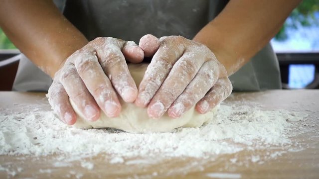 Female cook throws down loaf a dough and kneading on a table with green tree blurred background