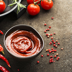Dark ceramic bowl with tomato sauce, fresh vegetables, herbs, pepper on a dark background. Top View.
