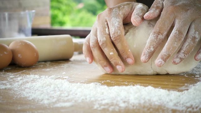 Female hands kneading dough in flour with green tree blurred background