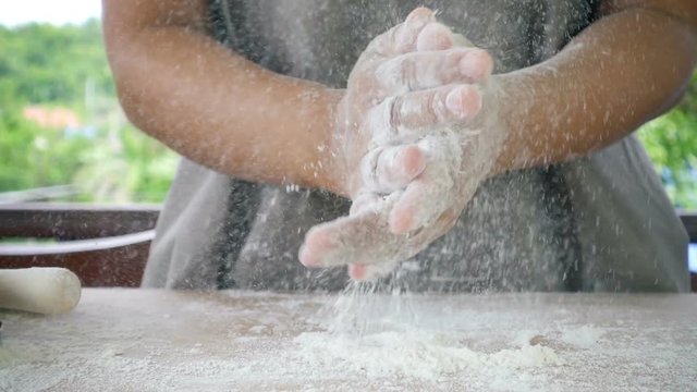Professional female cook claps her hands and powder flies. Concept: the production of sweets bread dough. Ingredients and preparation stages. Slowmotion shot.
