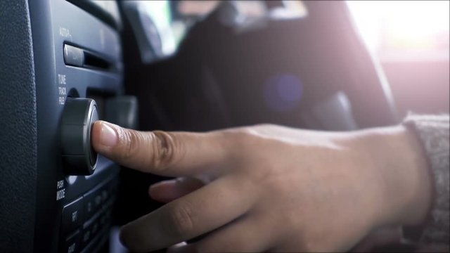 Close-up of female hand adjusting button audio on a vehicle's dashboard.