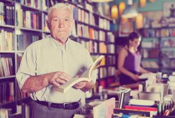 Senior male shopper is choosing book for reading