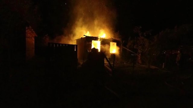 unrecognizable firemen extinguish fire at the wooden house at night