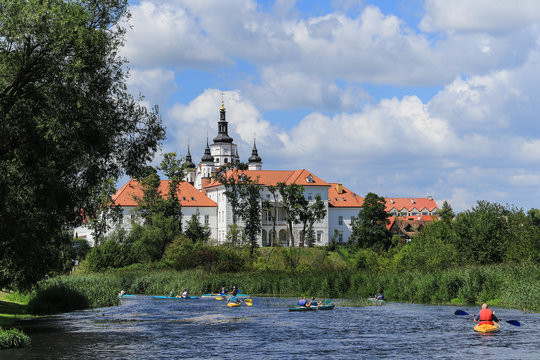 Group of people canoeing on the Narew river at the bottom of the hill with the monastic complex with defensive features from 16th and 17th century, Podlasie region, Suprasl, Poland