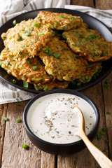 Homemade zucchini fritters with greens and sour cream close-up. vertical