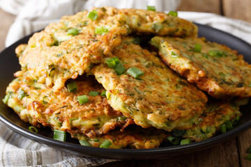 Hot zucchini pancakes with green onions on a plate close-up on a table. Horizontal