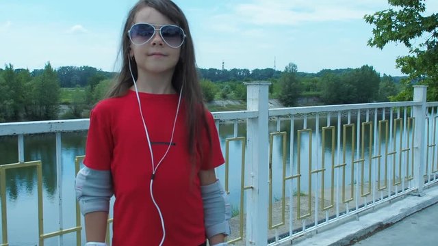 A little girl on the rollers listens to music. A child in the headphones listens to music.