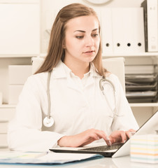 Doctor woman in uniform is working behind laptop